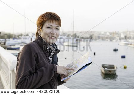 Woman With Short Red Haircut Reads Malta Map. Curious Woman Stands Near Msida Yacht Marina. Europe T