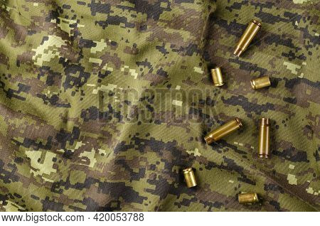 A Few Random Casings On Camouflage Cloth. A Group Of Pistol And Rifle Empty Casings Lie On Military 