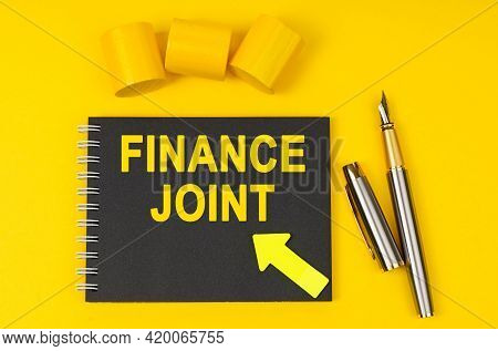 Business And Finance Concept. On A Yellow Background Lies A Pen, A Black Notebook With The Inscripti