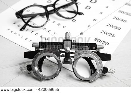 Trial Frame, Eye Chart Test And Glasses On White Wooden Table. Ophthalmologist Tools