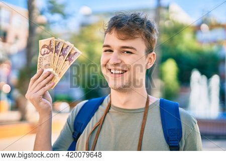 Young caucasian tourist man smiling happy holding hungarian forint banknotes at the city.