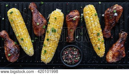 Top Down View Of Barbecue Chicken Legs And Corn On The Cob On A Grill Pan Topped With Green Onion An