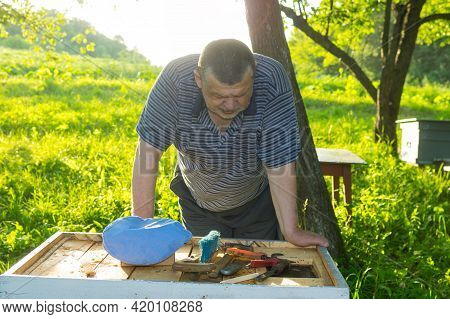Outdoor Portrait Of Caucasian Elderly Bee-keeper Stooped Down To Hive An Apiary And Thinking