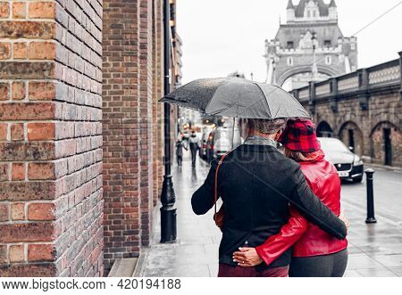 Couple Walking In The Rain Under A Beautiful Tower Bridge Of London. Retired Couple Traveling Around