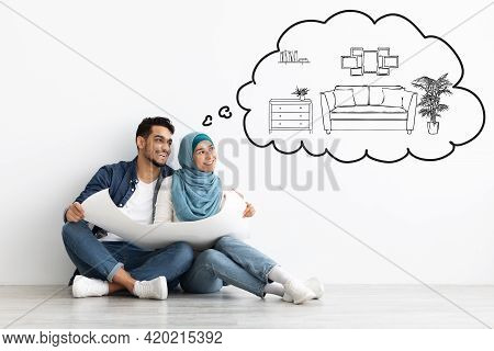 Dreaming Muslim Couple Sitting On Floor In Empty Apartment