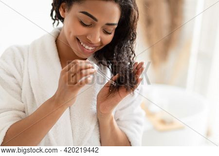 African American Woman Applying Serum On Damaged Hair In Bathroom