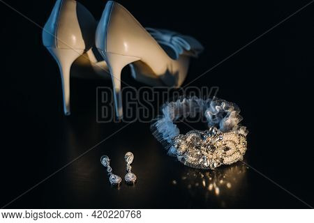 White Wedding Shoes And Garter Belt With Earrings On A Black Background