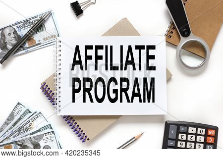 Affiliate Program. Notebook On White Workspace. Near The Notepad Dollar Bills And A Calculator
