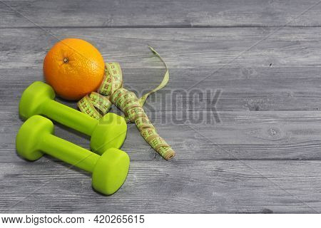 One Orange, Dumbbells, Measuring Tape On A Wooden Textured Background. Fitness, Sports Nutrition.