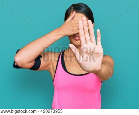 Beautiful asian young sport woman wearing sportswear and arm band covering eyes with hands and doing stop gesture with sad and fear expression. embarrassed and negative concept. 