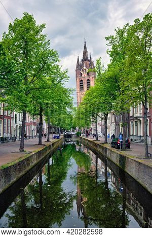 Delt canal with old houses bicycles and cars parked along and Oude Kerk Old church tower. Delft, Netherlands