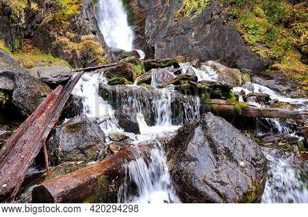 A Rushing Stream Of A Small Mountain River Skirting Stones And Dumped Tree Trunks.