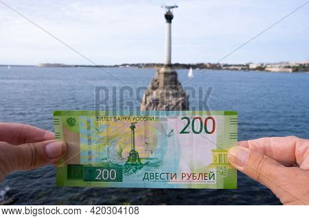 Banknote Of 200 Russian Rubles In Womens Hands Against The Background Of The Monument To Sunken Ship