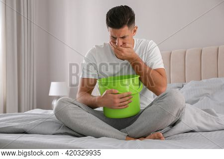 Man With Bucket Suffering From Nausea On Bed At Home. Food Poisoning