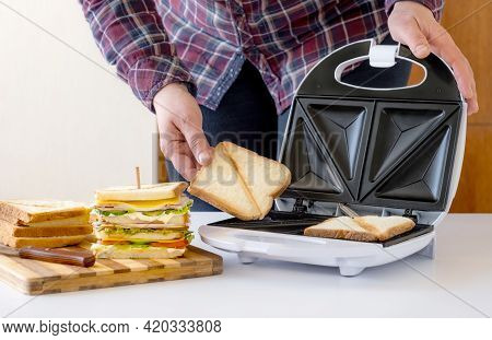 Hand Holds Fried Slice Of Bread From The Toster Near Cooked Fresh Sandwich With Cheese, Bacon And Ve
