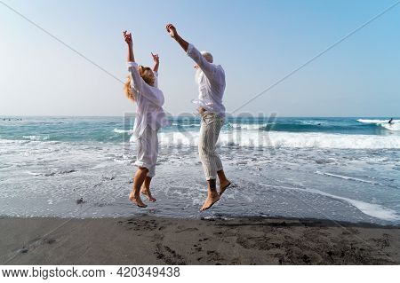 Lifestyle With Caucasian Senior Couple Jump Fun On Beach, Happy In Love Romantic And Relax Time, Tou