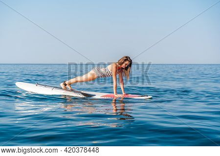 Sporty Girl On A Glanders Surfboard In The Sea On A Sunny Summer Day. In A Striped Swimsuit, It Is I