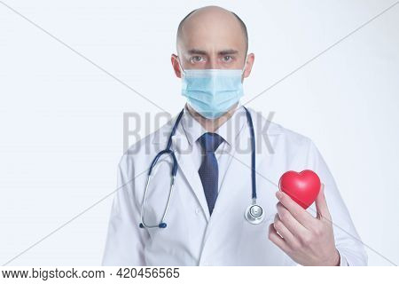 Doctor In Protective Mask And Medical Stethscope Hold Heart In His Hand. Isolated In White Backgroun