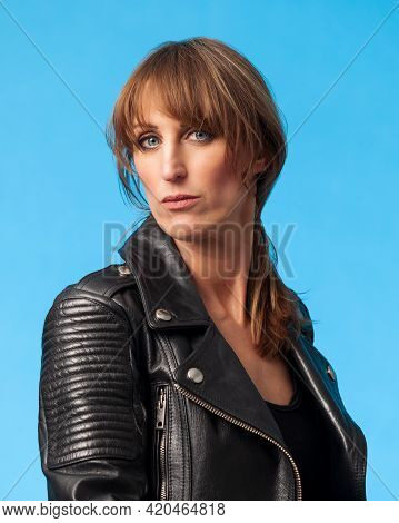 Portrait Of A Beautiful Blonde Woman Wearing A Black Leatherjacket Against A Blue Background
