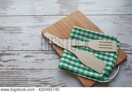 Wooden cutting board, white and green kitchen napkin, wooden spatula on a wooden background. View from above