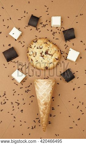 Overhead Shot Of An Ice Cream Cone With A Chookie Surrounded By Pieces Of Chocolate, On A Brown Back