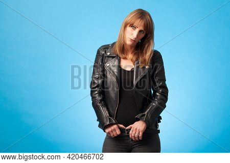 Portrait Of A Beautiful Blonde Woman Wearing A Black Leatherjacket Against A Blue Background