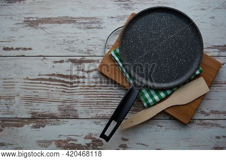 Empty frying pan, green and white kitchen napkin, wooden spatula, wooden cutting board isolated on wooden background. Copyspase