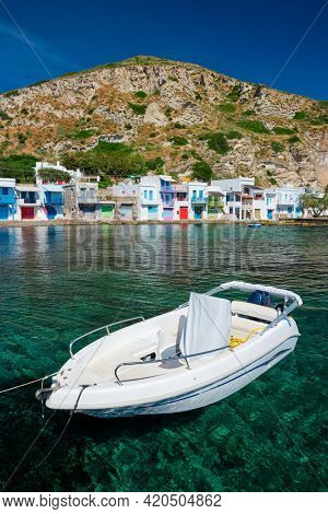 Greek fishing boat in the Aegean sea with picturesque scenic greek Klima village in background, Milos island, Greece