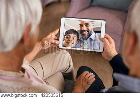 Senior couple doing a video call with son and grandson during covid19 pandemic. Happy indian father with child greeting in video conference his parents. Hands of old grandparents using digital tablet.
