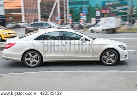 Side View Rolling Shot With White Car In Motion. Mercedes-benz Cls Class Driving Along The Street In