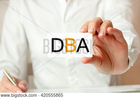 A Woman In A White Shirt Holds A Piece Of Paper With The Text: Dba. Dba - Doctor Of Business Adminis