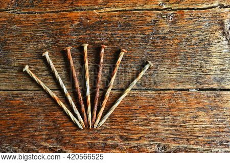 A Close Up Image Of Several Old And Rusted Carpentry Nails On A Dark Wooden Nails.