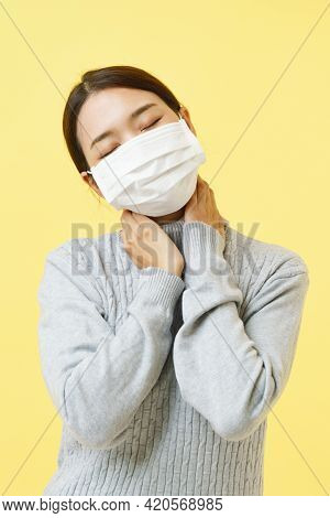 Asian Woman Wearing Flu Or Surgical Mask Show Neckache Over Yellow Background.