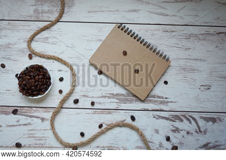 Brown Notepad, Coffee Beans, Whip On Wooden Background. Top View