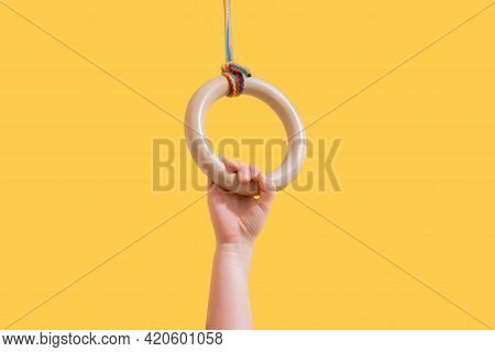 A Kid Hangs By One Hand On A Gymnastic Ring Isolated On A Yellow Background. Orange. Competitor. Sch