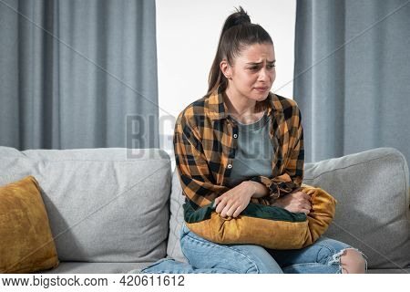 Young Woman With Menstruation Is Sitting On The Couch And Holding On To Her Stomach Because She Is I