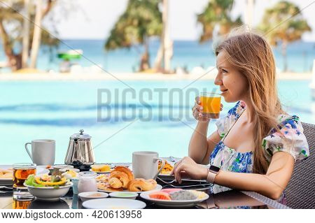 Smiling Woman On American Breakfast Drinking Orange Juice Next To Poolside In Resort. Morning Food N