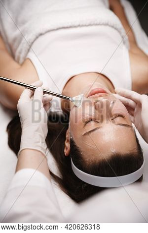 Beautician Using Cosmetology Brush To Apply Galvanic Gel On Female Client Lying On Therapy Table Bea
