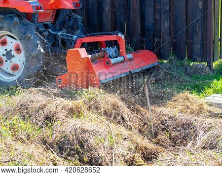 A Tractor With A Mower Attached Mulches Dry Grass Along The Fence. Land Plot Processing