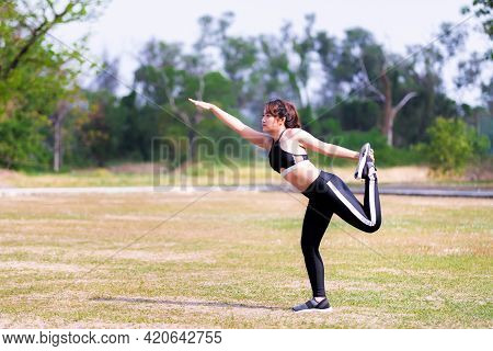 Woman Doing Yoga Exercises On The Lawn. Person Stands On One Leg, Extending The Right Arm Forward, T