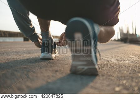 Closeup Of Man Tying Shoe Laces On The Road Before Running In Sunset. Sport And Workout Concept.