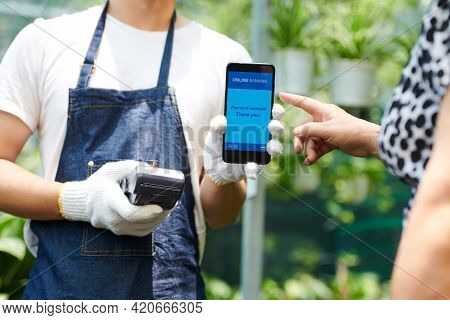 Greenhouse Worker In Protective Gloves Holding Teminal And Accepting Contactless Payment From Custom