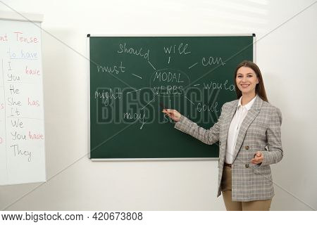 English Teacher Giving Lesson On Modal Verbs Near Chalkboard In Classroom