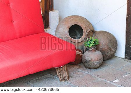 Large Vintage Decorative Clay Pots Next To A Red Sofa In The Shade