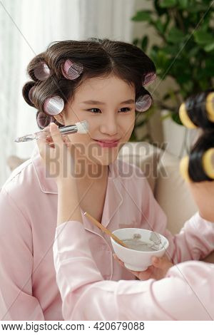 Smiling Pretty Young Woman Getting Mud Mask Applied On Her Face With Synthetic Brush