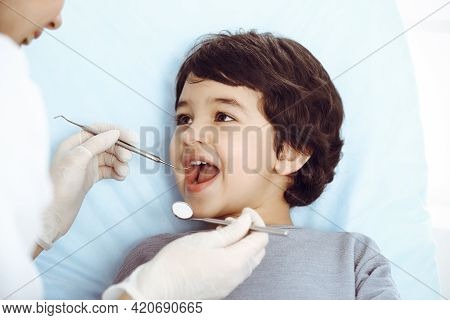 Cute Arab Boy Sitting At Dental Chair With Open Mouth During Oral Checking Up With Doctor. Visiting 