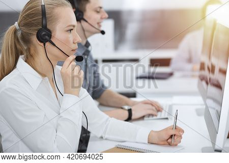 Call Center. Group Of Casual Dressed Operators At Work. Blond Business Woman In Headset At Customer 