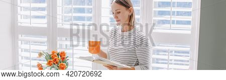 Beautiful Happy Middle Age Woman Reading Book At Home. Young Woman With Short Hair Drinking Tea Coff