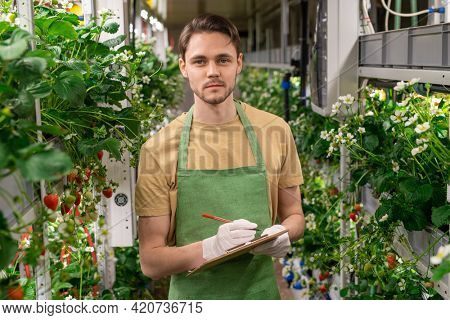 Young male farmer with pen and clipboard making notes in verical farm