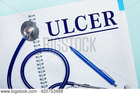 On A Light Blue Background, An Open Notebook With The Word Ulcer, A Blue Pen And A Stethoscope. View